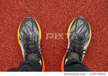 Close-up of an athlete's feet wearing colorful running shoes on red track surface, ready for workout. Sportsman legs in sport sneakers, close up. Fitness and healthy lifestyle 120570009