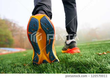 Close-up of running shoes sole with athlete walking on artificial grass. Sportsman legs in sport sneakers on green grass Close-up of running shoes sole with athlete walking on artificial grass. Sportsman legs in sport sneakers on green grass 120570011
