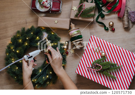 Top view of a woman using a glue gun to glue toys to a Christmas wreath. Holliday mood Top view of a woman using a glue gun to glue toys to a Christmas wreath. Holliday mood 120571730