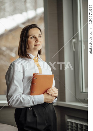 professional woman standing near a window, exuding confidence and focus, natural light and create a calm atmosphere 120571955