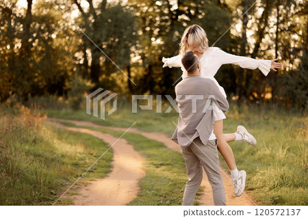 Young happy couple walking in the park. A man circles a woman in his arms. Young happy couple walking in the park. A man circles a woman in his arms. 120572137