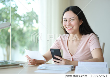 Asian woman holding bill and phone looks at you Asian woman holding bill and phone looks at you 120572971
