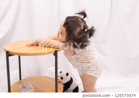 [Baby with twin tails standing up holding onto a table] 120573074