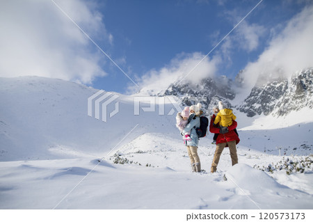Young family is enjoying winter holiday in the mountains, standing in the middle of snowy landscape. Young family is enjoying winter holiday in the mountains, standing in the middle of snowy landscape. 120573173