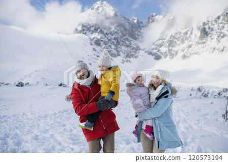 Young family is enjoying winter holiday in the mountains, standing in the middle of snowy landscape. Young family is enjoying winter holiday in the mountains, standing in the middle of snowy landscape. 120573194