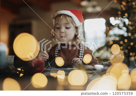Portrait of small girl indoors at Christmas home. Girl painting picture for Santa Claus or making christmas decoration. 120573359