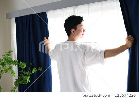 Asian man opening the curtains and basking in the sunlight Asian man opening the curtains and basking in the sunlight 120574226