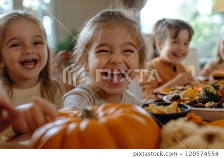 A young girl laughing with a pumpkin in front of her while eating dinner with her family 120574554