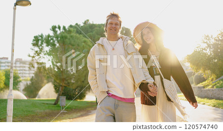 A lovely couple enjoys a carefree walk together in the warm sunlight at the park today A lovely couple enjoys a carefree walk together in the warm sunlight at the park today 120574740