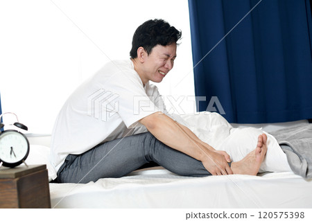 Asian man suffering from leg pain on bed 120575398