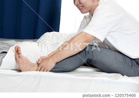 Asian man suffering from leg pain on bed 120575400