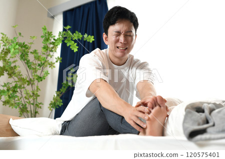 Asian man suffering from leg pain on bed 120575401