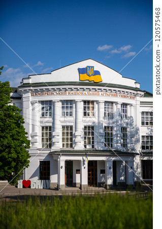 The photo shows a white building with columns, the Ukrainian flag, and the name "Bila Tserkva National Agrarian University." A sign reading "I love BNAU" is visible in the foreground. 120575468