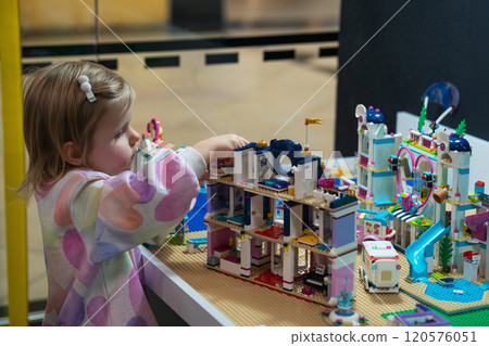 Kids Play Room. Cute girl child plays with colored plastic parts of the constructor, creates buildings, equipment, transport, the concept of the development of creativity, fine motor skills. Kids Play Room. Cute girl child plays with colored plastic parts of the constructor, creates buildings, equipment, transport, the concept of the development of creativity, fine motor skills. 120576051