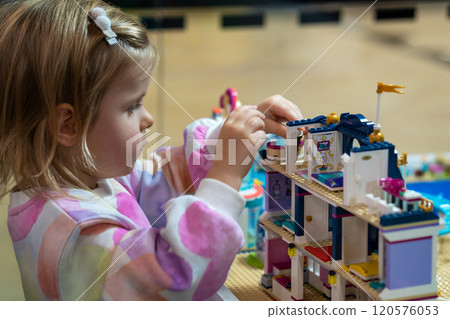 Kids Play Room. Cute girl child plays with colored plastic parts of the constructor, creates buildings, equipment, transport, the concept of the development of creativity, fine motor skills. Kids Play Room. Cute girl child plays with colored plastic parts of the constructor, creates buildings, equipment, transport, the concept of the development of creativity, fine motor skills. 120576053