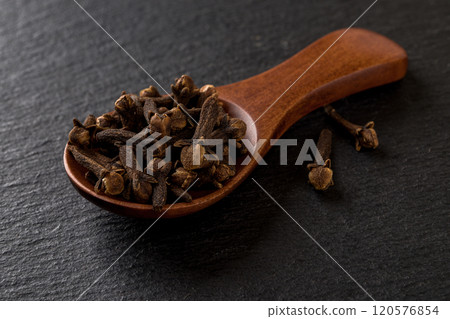 Whole cloves spice in a wooden spoon over black background.  120576854