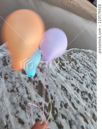 Three colorful inflatable balls on background of sea during strong winds. Person playing with multi-colored air balloons in hand on background sea waves on sandy beach of seashore. Entertainment fun 120576928