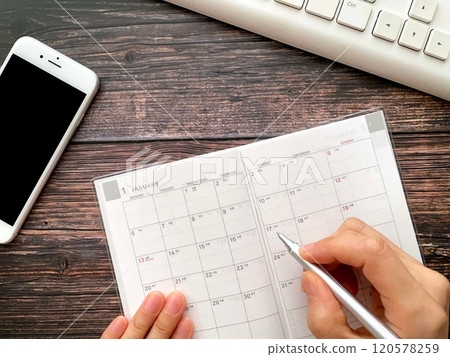 A woman's hand filling out a schedule book for January 120578259