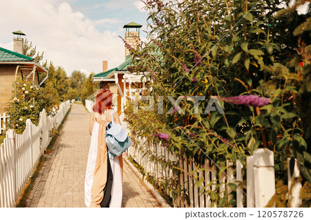 A woman carrying a backpack strolls leisurely along a picturesque pathway that is beautifully lined with lush greenery 120578726