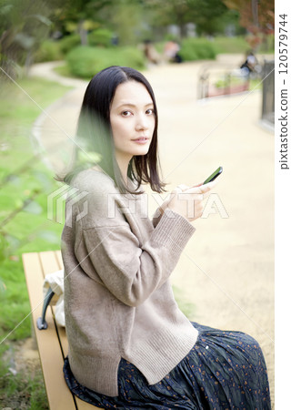一個女人在公園長椅上看智能手機 120579744