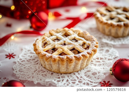 Intricately designed mince pies resting on a lace napkin, surrounded by cheerful red ribbons, evoking holiday warmth 120579816