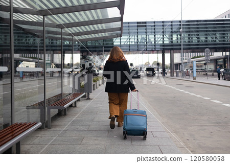 Traveler businesswoman with suitcase calling mobile phone waiting taxi on road in city street. Charming girl moves near airport with luggage. 120580058