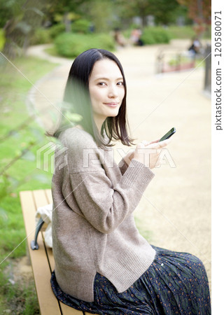 A woman looking at a smartphone on a park bench 120580071