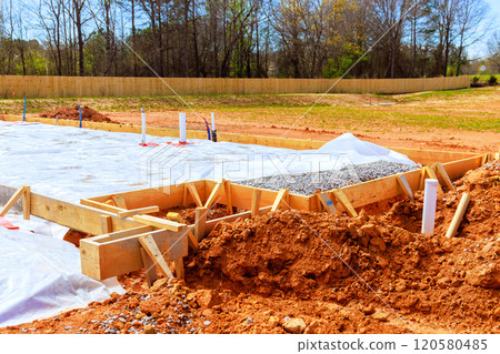 Preparing foundation at construction site with wooden forms filled with gravel surrounded by covered area with protective plastic to prevent moisture 120580485