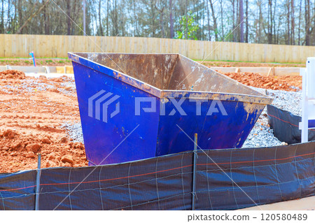 Dumpster sits on construction site surrounded by dirt gravel area is partially cleared 120580489