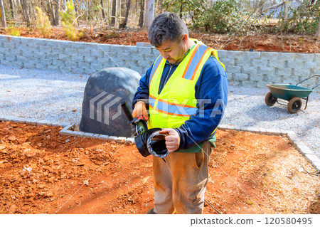Worker wearing safety vest is cuts off part of drainage pipe before installation at during construction site 120580495