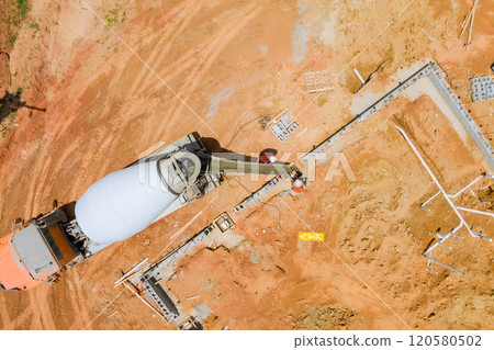 Worker pouring concrete along foundations in spacious area with reddish soil using concrete mixer truck. Worker pouring concrete along foundations in spacious area with reddish soil using concrete mixer truck. 120580502