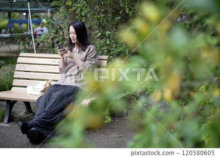 A woman looking at a smartphone on a park bench A woman looking at a smartphone on a park bench 120580605