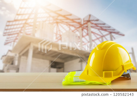 Yellow safety construction helmet on wood table with construction site background 120582143
