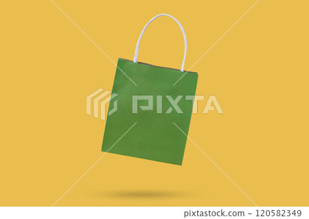 Green paper shopping bag isolated on yellow background 120582349