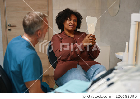 Smiling Patient Holding Mirror during Dental Checkup 120582399
