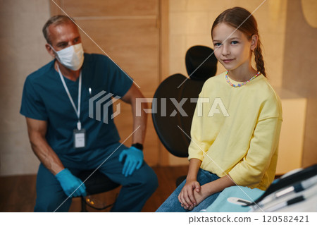 Smiling Girl Sitting in Dental Office With Dentist Nearby Smiling Girl Sitting in Dental Office With Dentist Nearby 120582421