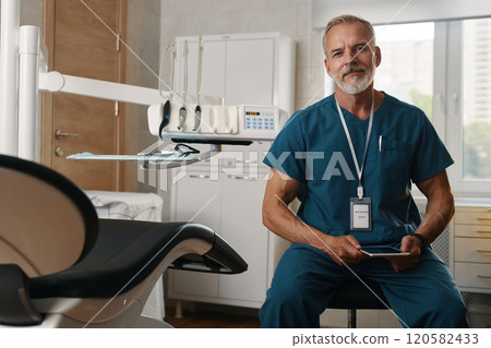 Portrait of Smiling Dentist Sitting in Modern Dental Clinic 120582433