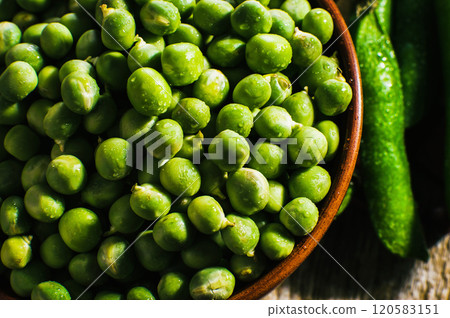 Beans and pods of green peas are in a bowl on a wooden surface.green sweet peas on a dark wooden background, still life, concept of fresh and healthy food Beans and pods of green peas are in a bowl on a wooden surface.green sweet peas on a dark wooden background, still life, concept of fresh and healthy food 120583151
