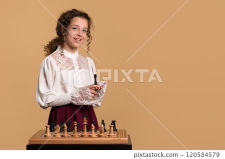 Young girl smiling while holding chess piece in hand. 120584579