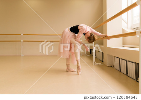 Ballet dancer leaning on barre, stretching in pink tutu 120584645