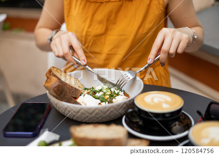 Woman eating tasty Shakshuka at cafe. Middle eastern traditional dish. Fried eggs with tomatoes and cup of coffee. Concept of easy breakfast. Food banner Woman eating tasty Shakshuka at cafe. Middle eastern traditional dish. Fried eggs with tomatoes and cup of coffee. Concept of easy breakfast. Food banner 120584756