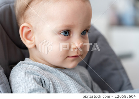 Cute baby with soft expression and blue eyes in gray outfit. Concept of youthful innocence and peaceful mood 120585604