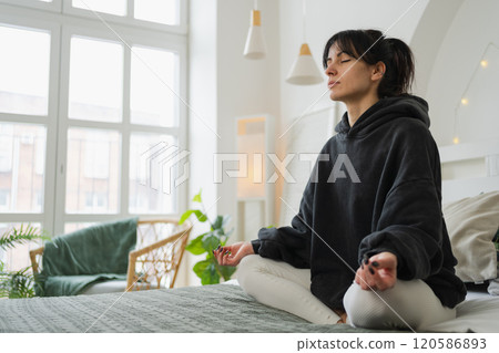 Yoga mindfulness meditation. Young healthy woman practicing yoga in bedroom at home. Woman sitting in lotus pose on bed meditating smiling relaxing indoor. Girl doing breathing practice. Yoga at home 120586893