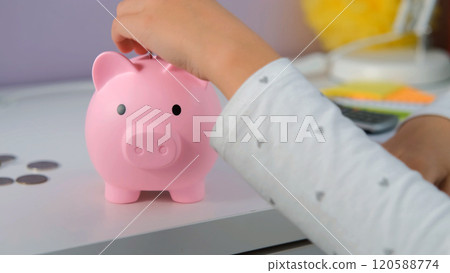 Close-up of a young girl concentrates as she places coins into her piggy bank, practicing personal finance skills and understanding the importance of saving 120588774
