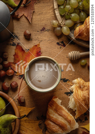 Cozy autumn breakfast composition with coffee, croissants, autumn fruits, grapes, pears and hazelnuts on wooden table. Top view Cozy autumn breakfast composition with coffee, croissants, autumn fruits, grapes, pears and hazelnuts on wooden table. Top view 120588994