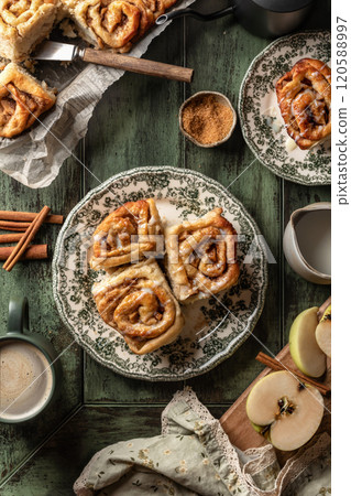 Autumn apple cinnamon rolls with frosting on green wooden background. Seasonal autumn homemade pastry cinnabons for breakfast Autumn apple cinnamon rolls with frosting on green wooden background. Seasonal autumn homemade pastry cinnabons for breakfast 120588997