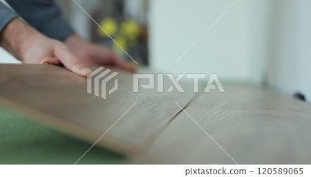 Man kneeling and installing wood laminate floor in a home. Closeup on male hands. 120589065