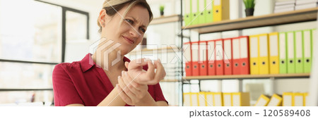 Tired woman employee kneads wrist and feels pain in office Tired woman employee kneads wrist and feels pain in office 120589408