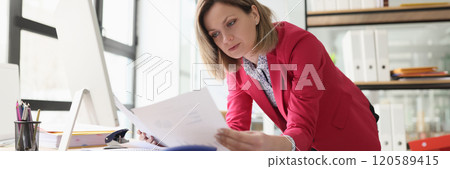 Concentrated blonde woman reads documents leaning on table 120589415
