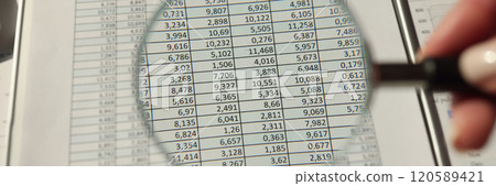 Hand of woman holds magnifier glass over accounting document 120589421